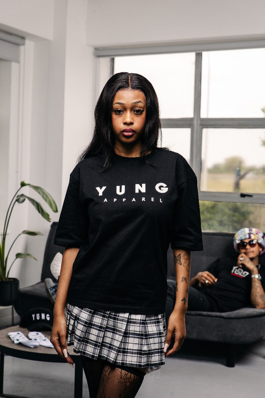 Woman wearing a black 'YUNG APPAREL' t-shirt in a modern living room.
South Africa