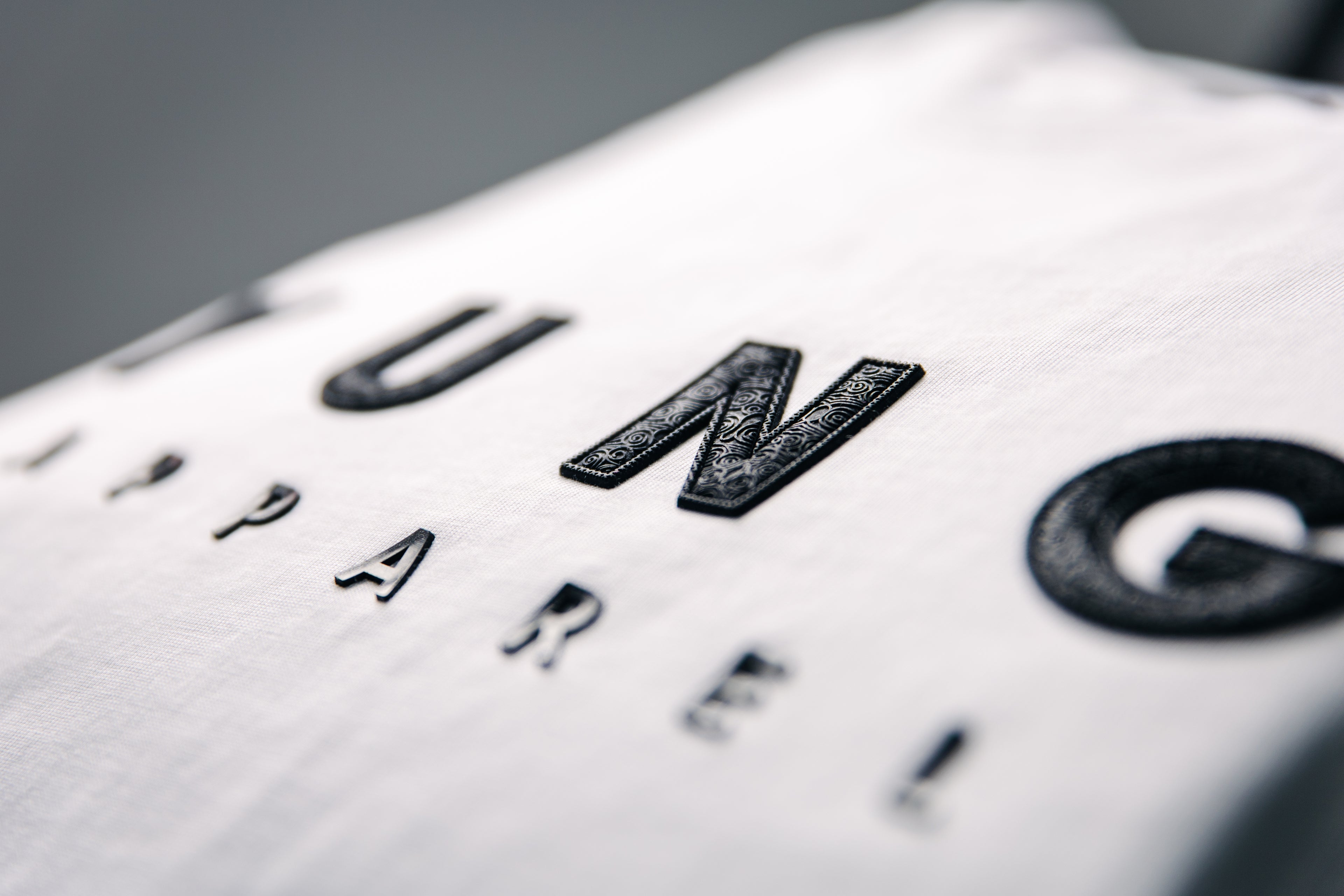 Close-up of a white YUNG T-shirt with embossed text on it written Y U N G APPAREL
South Africa