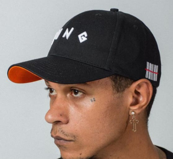 Person wearing a YUNG black cap with orange brim and visible barcode on the side on gray background
South Africa