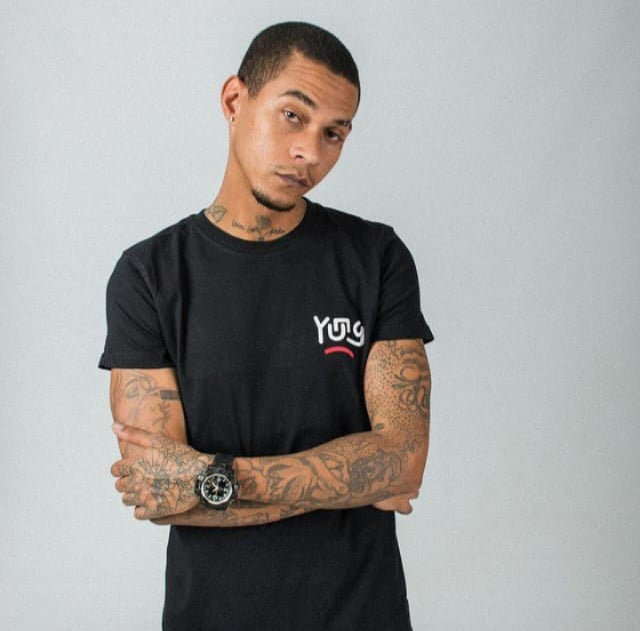 Man wearing aYUNG  black t-shirt with a logo, standing against a plain background