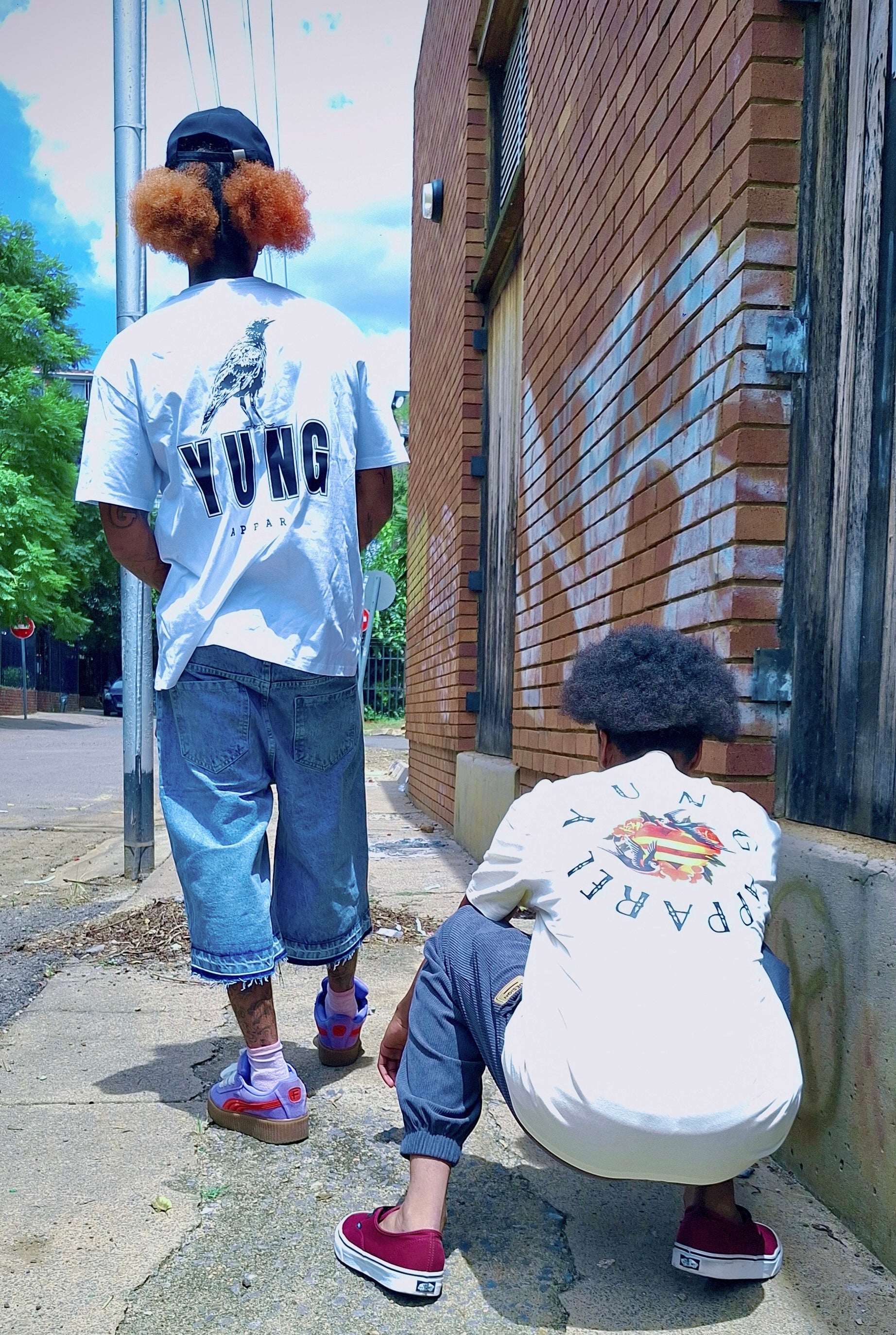 Two people wearing a YUNG APPAREL t-shirts with colorful designs and text, standing on a sidewalk.
South Africa