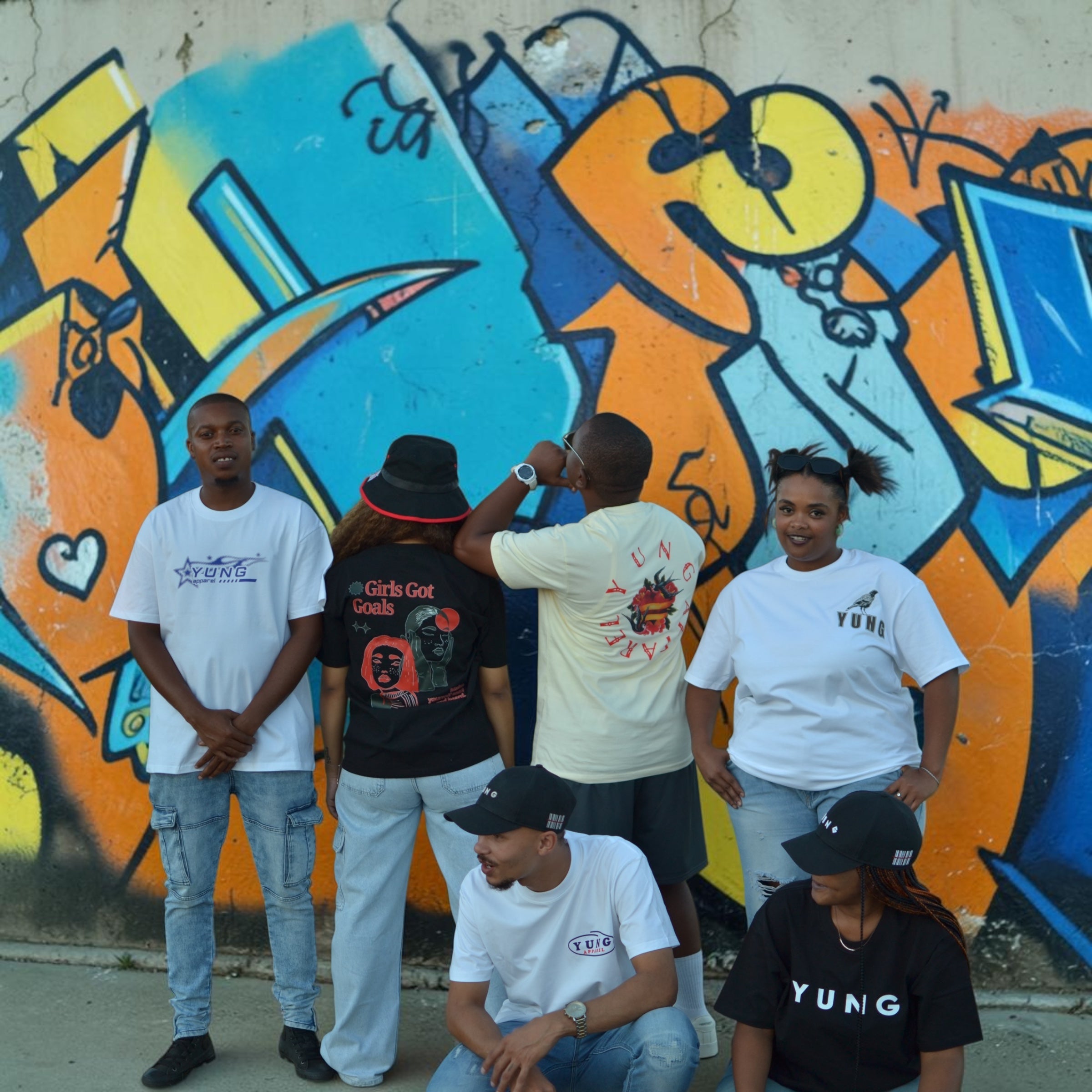 Group of people standing in front of a colorful graffiti wallwearing YUNG APPAREL T-shirts
South Africa