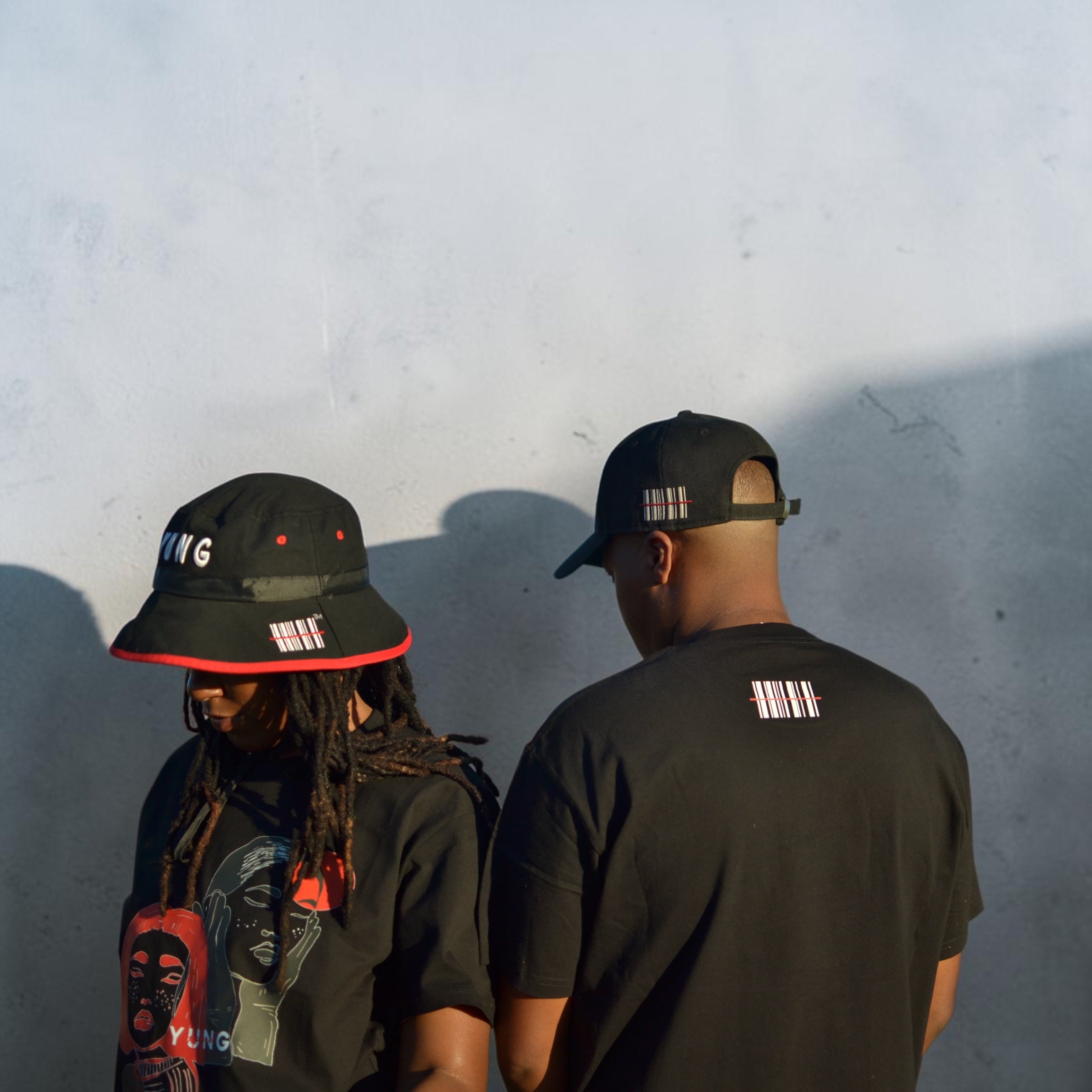 Two people wearing YUNG black hats and t-shirts against a light gray wall.
South Africa