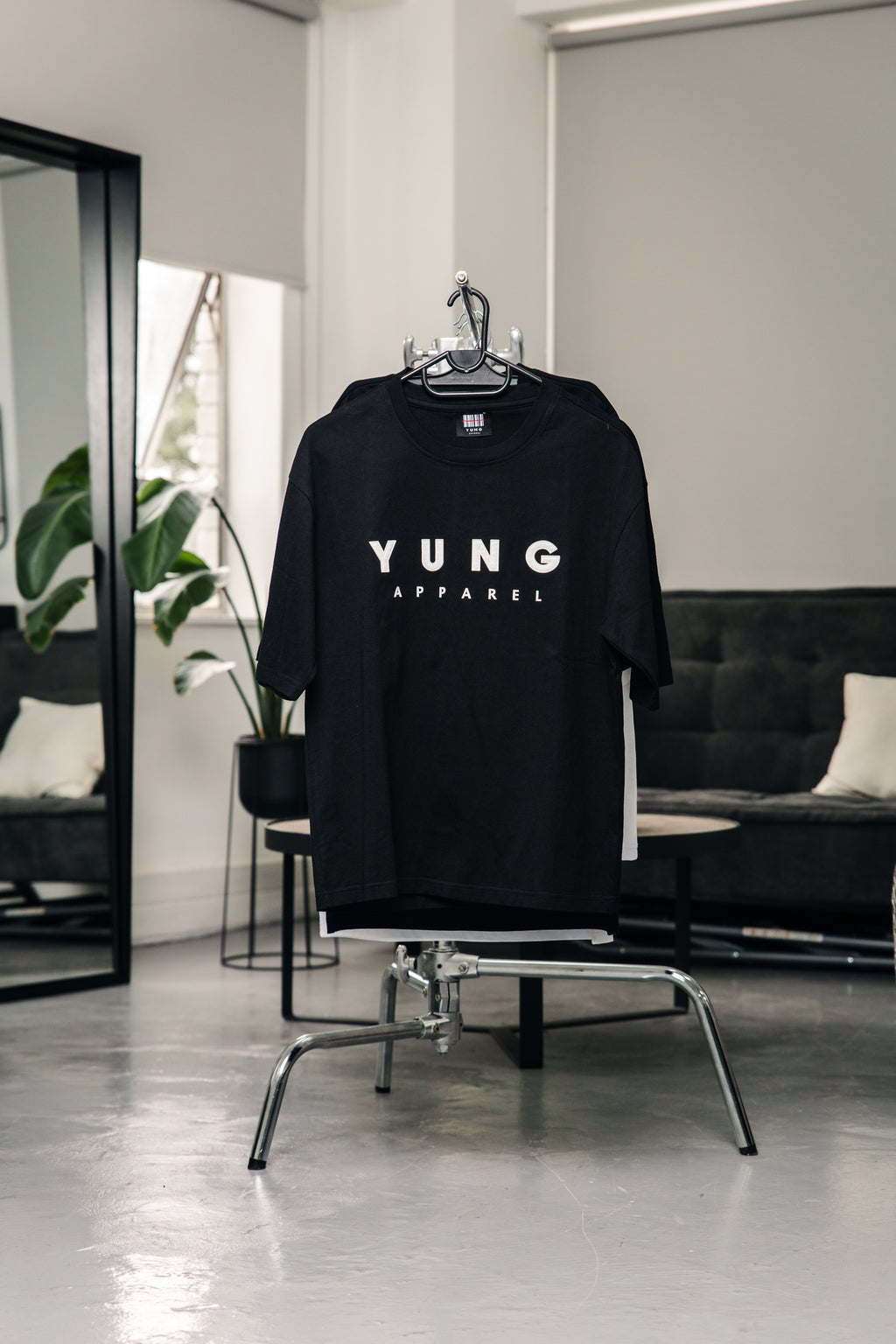 Black t-shirt with 'YUNG APPAREL' logo on a hanger in a room with a couch
Streetwear South Africa