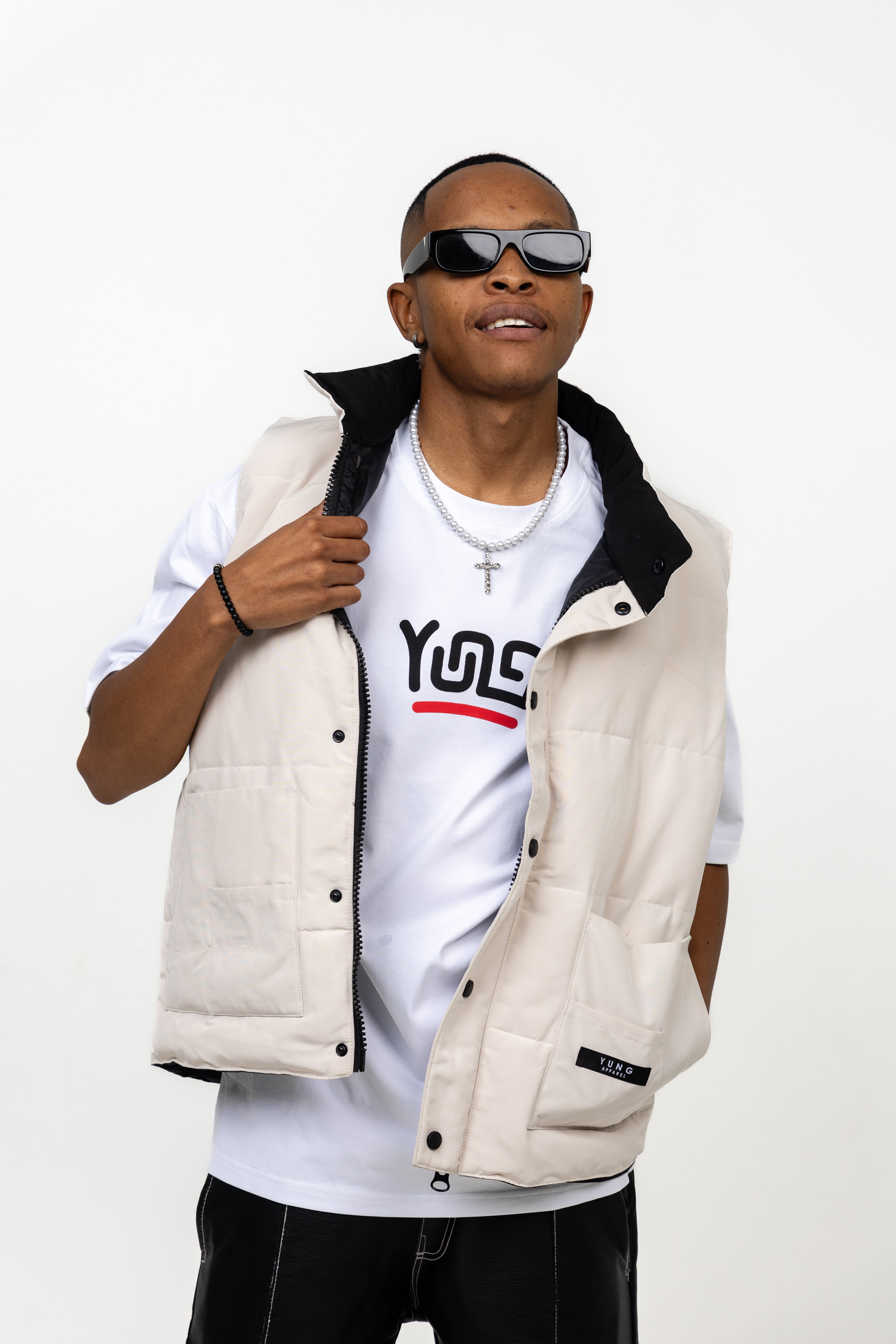 Man wearing a YUNG white sleeveless jacket over a YUNG white t-shirt, sunglasses, and black pants on a white background
South Africa