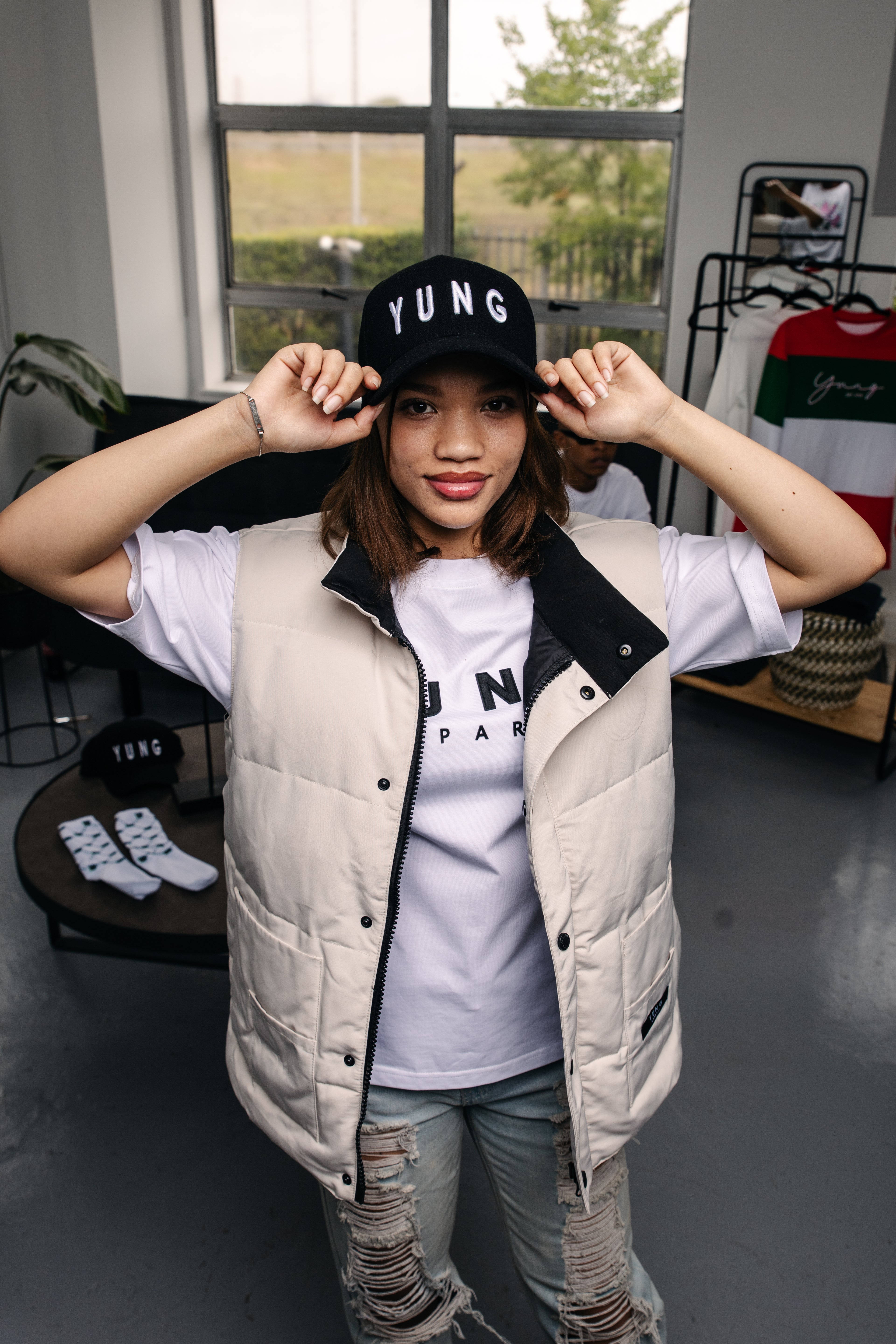 Person wearing a YUNG white puffer vest, YUNG black baseball cap, and a YUNG white t-shirt indoors.
South Africa
