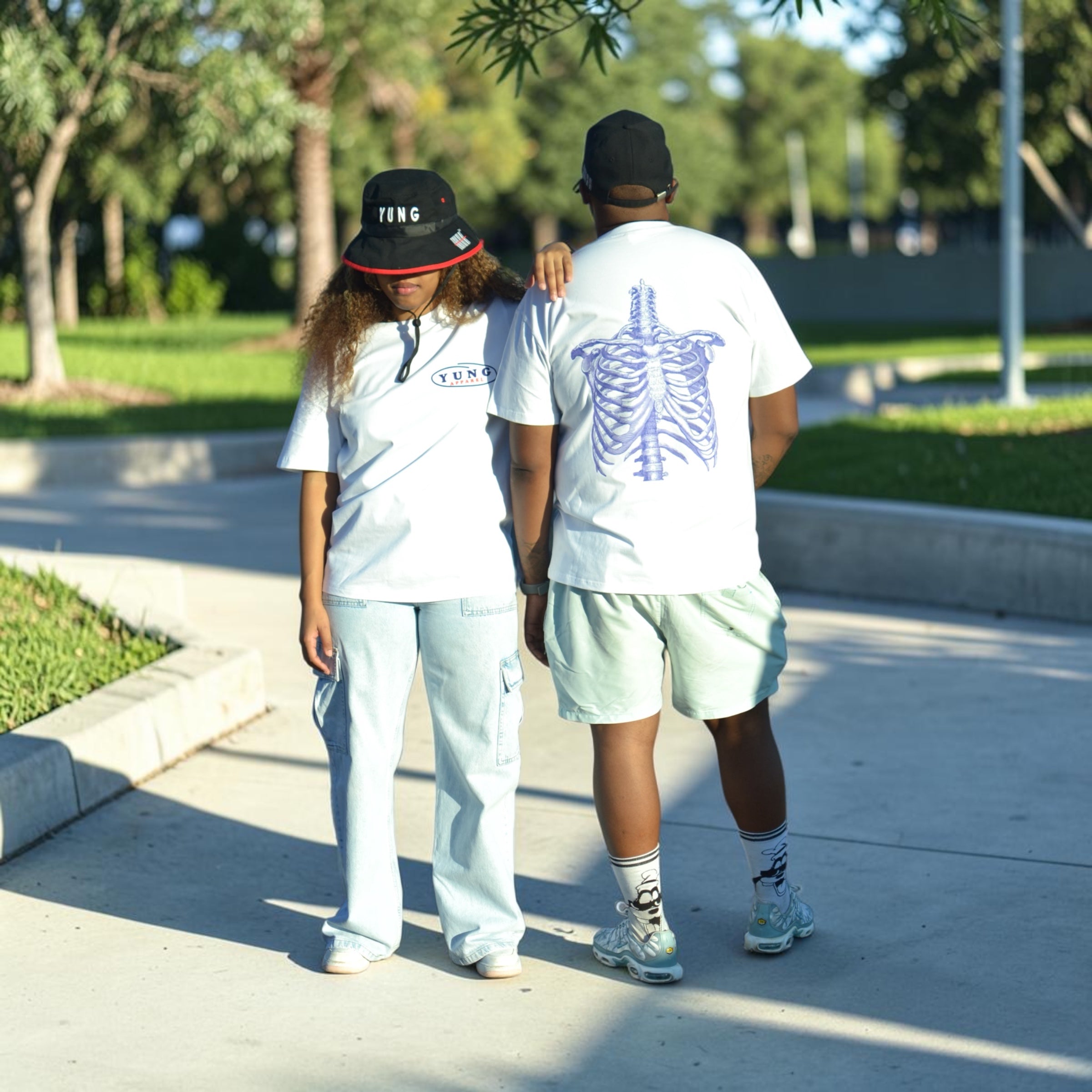 Two people walking on a sidewalk with trees and grass in the background wearing YUNG Tshirts
South Africa