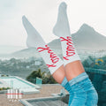 Person wearing YUNG white socks with red text and blue jeans, standing on a rooftop with a scenic view.
Streetwear South Africa