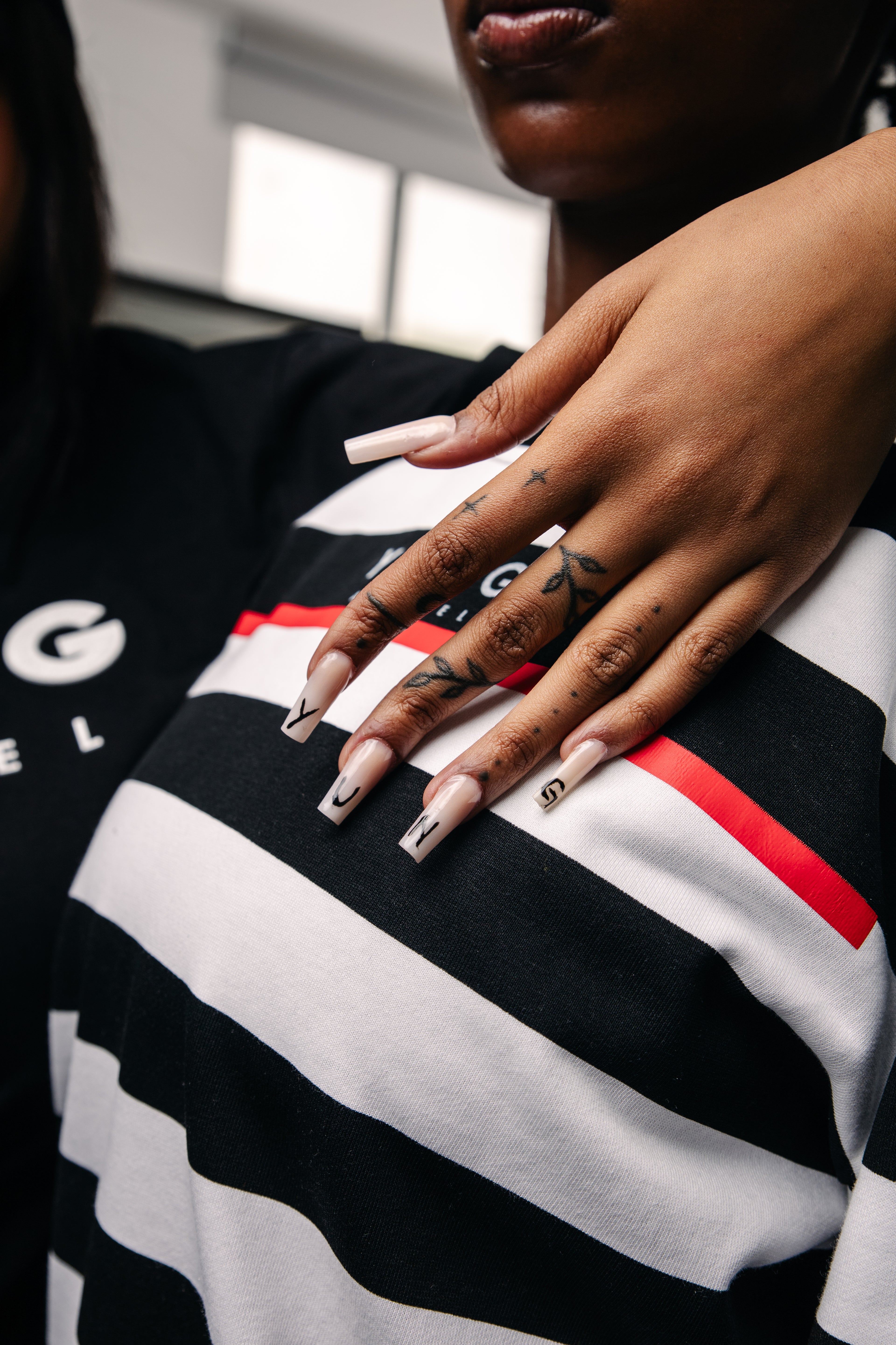 Person wearing a YUNG black, white, and red striped long sleeve t-shirt with visible tattoos on hands and YUNG nails
South Africa