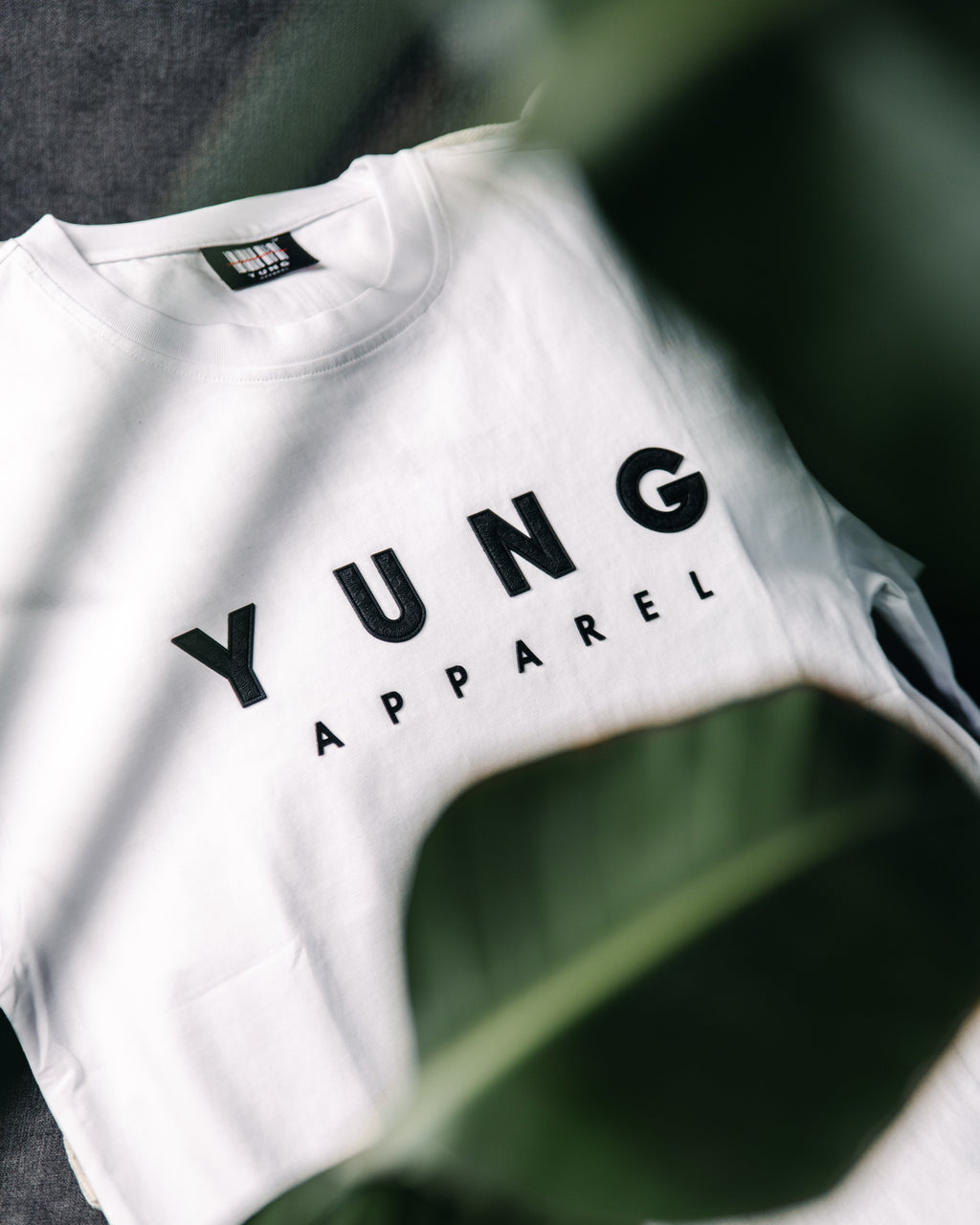 White t-shirt with 'YUNG APPAREL' text on a blurred green leaf background
Streetwear South Africa