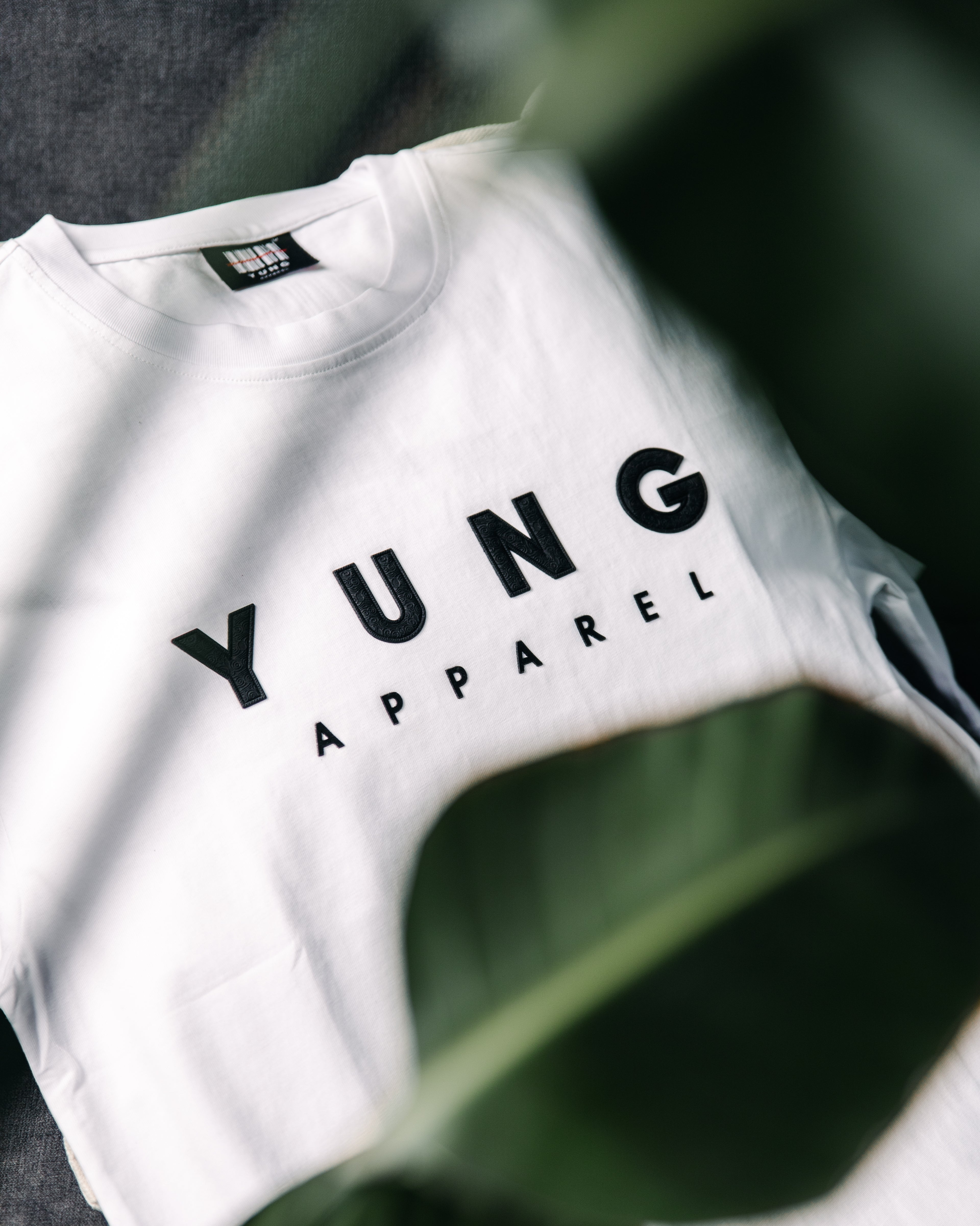 White t-shirt with 'YUNG APPAREL' text on a blurred green leaf background
Streetwear South Africa